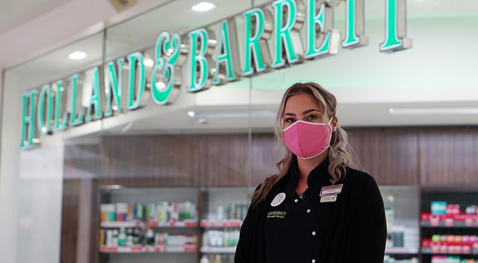 A Holland & Barrett colleague standing outside of a store wearing a face covering