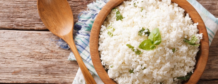 wooden bowl of fresh cauliflower rice with piece of basil 