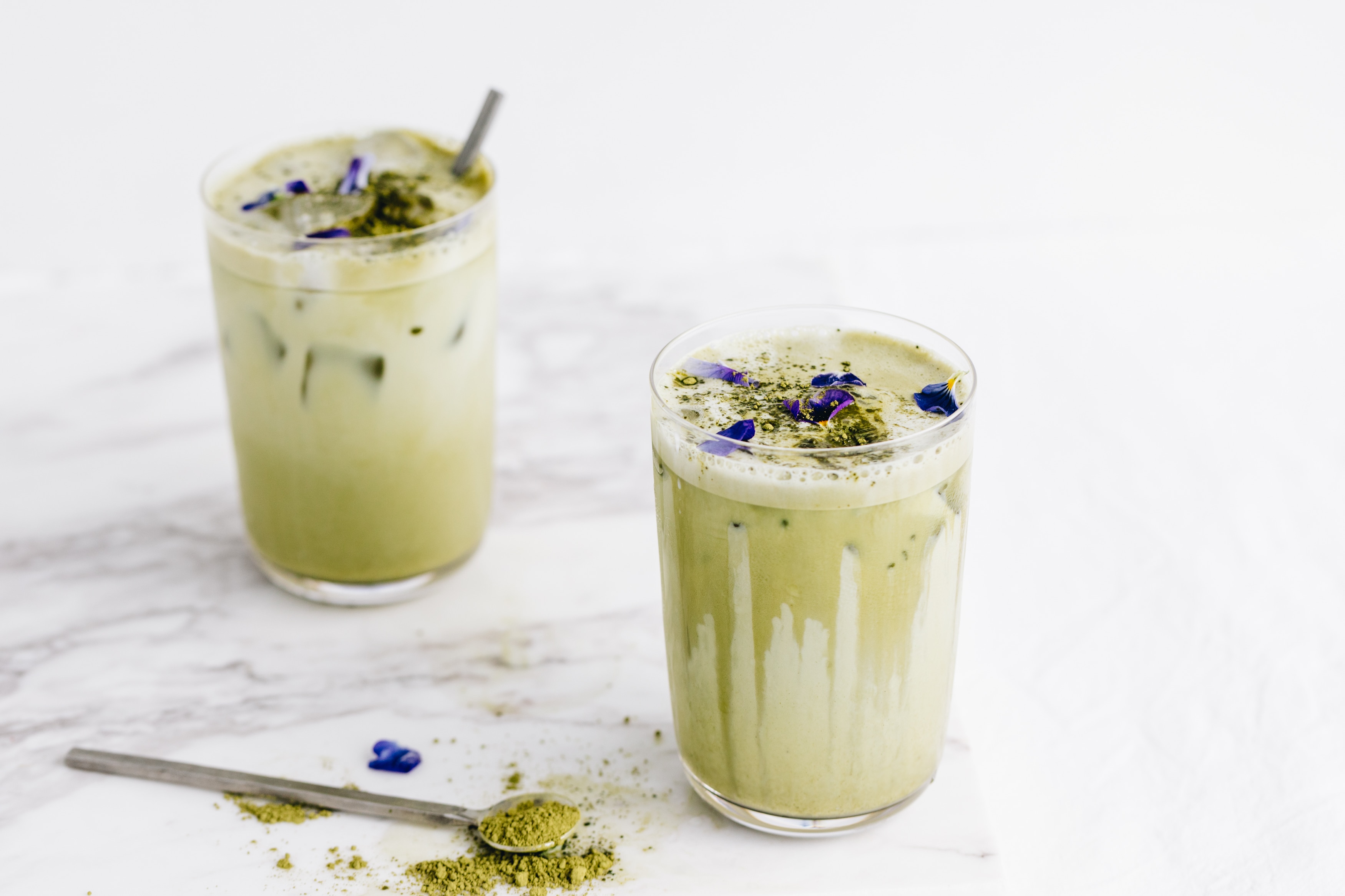matcha tea latte in two glasses with spoon of matcha powder
