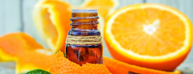 essential oil bottle with orange peel and orange in background