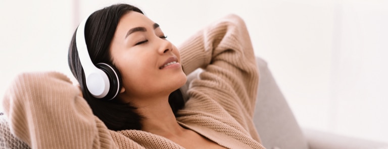 asian woman listening to podcast on headphones and relaxing