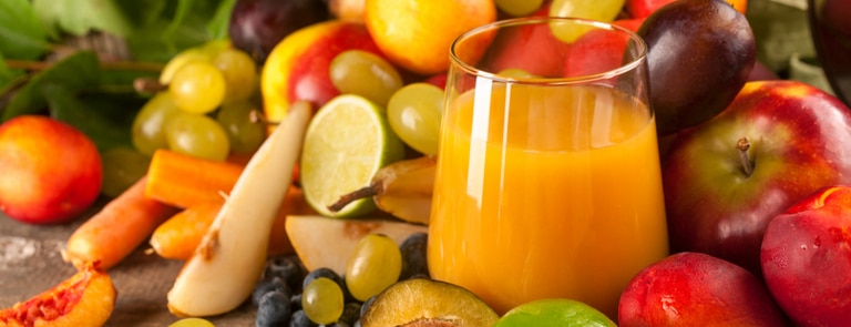 glass of orange juice surrounded by freshly cut fruit 