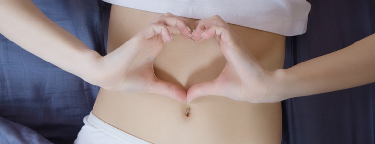 woman with hands in heart shape over stomach