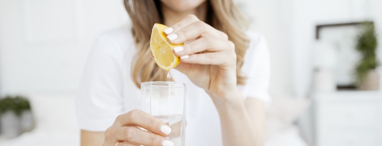 woman squeezing lemon into water glass