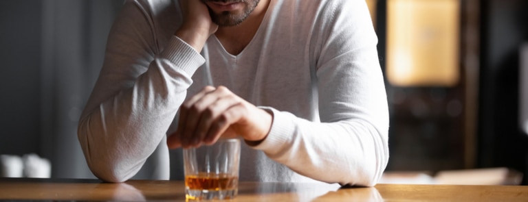 upset man sitting alone with glass of whiskey