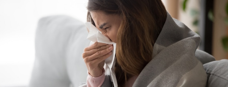 woman with flu in blanket sneezing in tissue