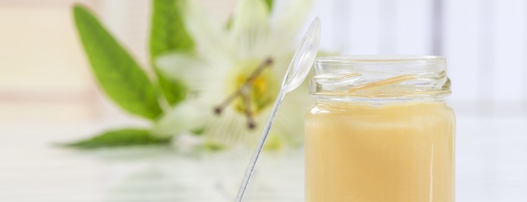 glass jar of royal jelly with flower in background