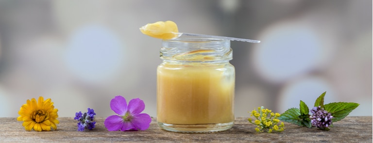 glass jar of royal jelly with flowers on wooden table