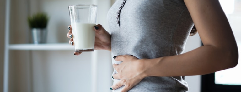 Woman holding a glass of milk and a sore stomach 