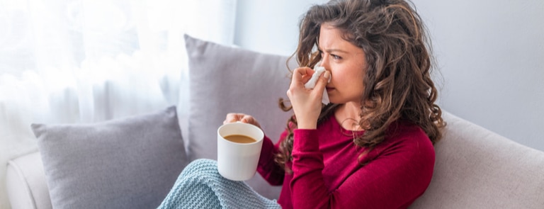 woman sat on the sofa with a cup of tea and a cold