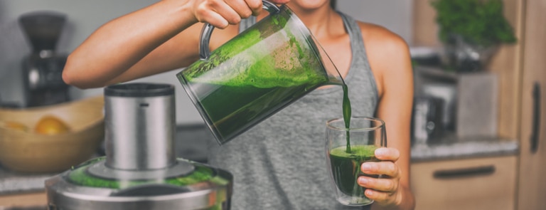 woman in kitchen pouring homemade green juice for juice diet
