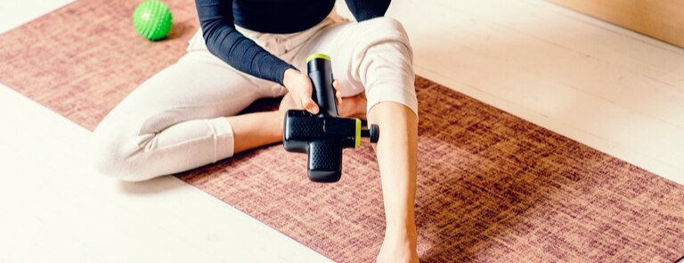 woman using massage gun on leg