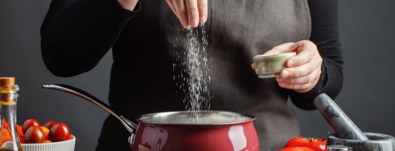 person putting salt into a their cooking 