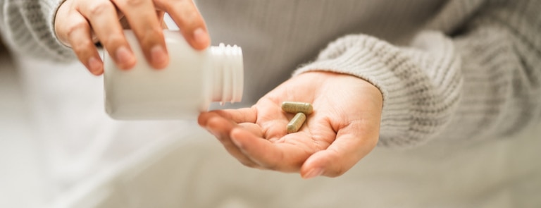 person tipping supplements out of a bottle 