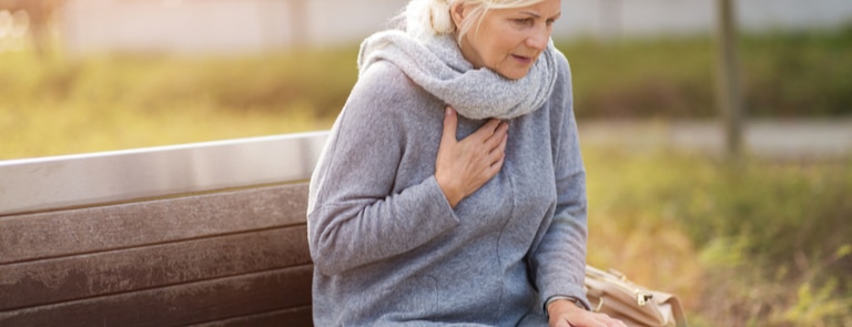 woman sitting on bench experiencing chest pain from heart disease
