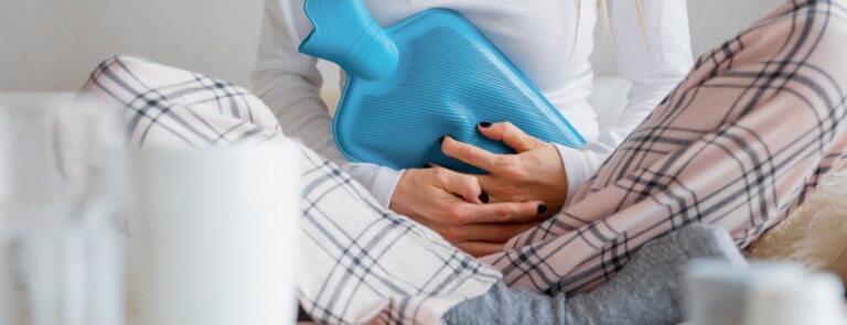 closeup of woman experiencing period pain placing hot water bottle on stomach