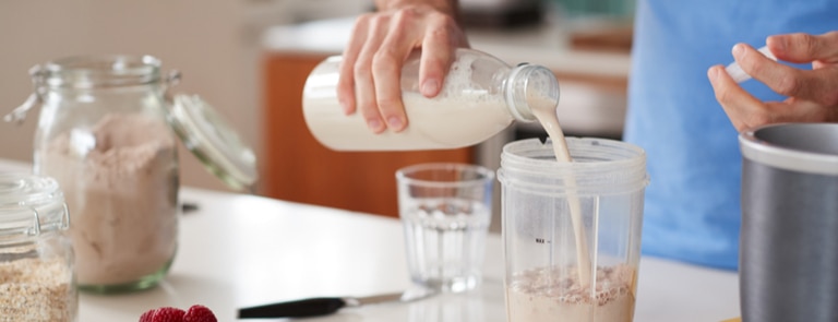 person pouring a protein drink in a glass