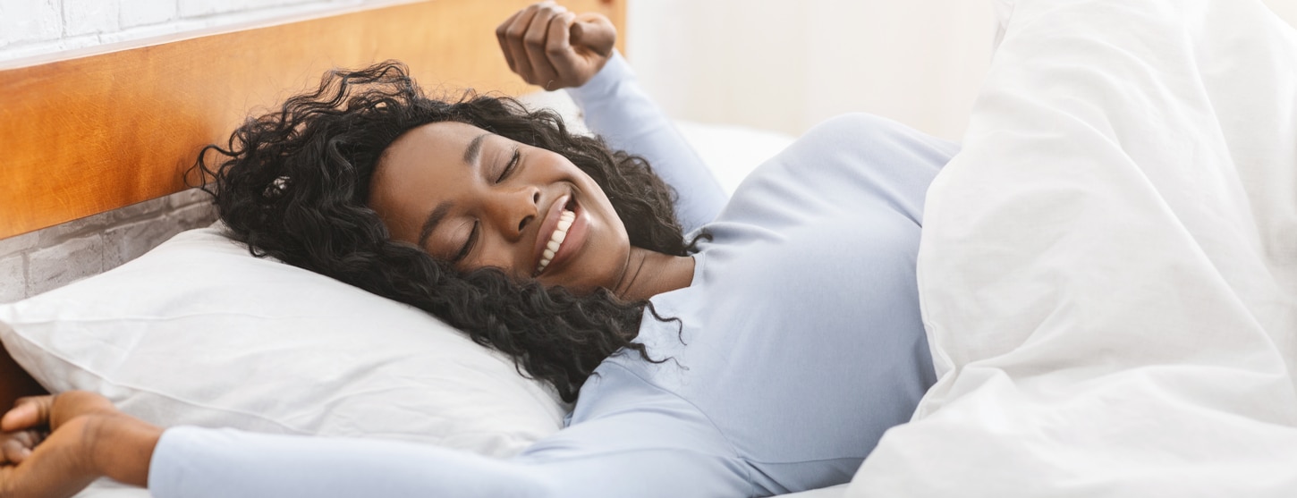 woman smiling in bed after having a full night of beauty sleep 