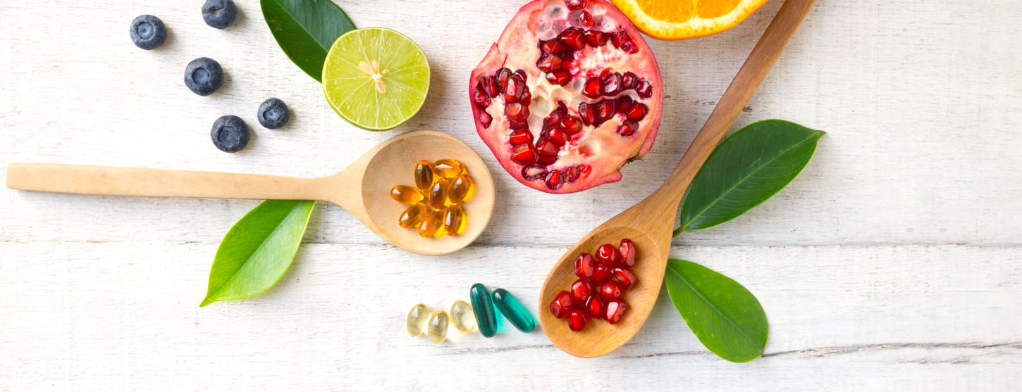 wooden spoon of vitamins next to pomegranate seeds and lime 