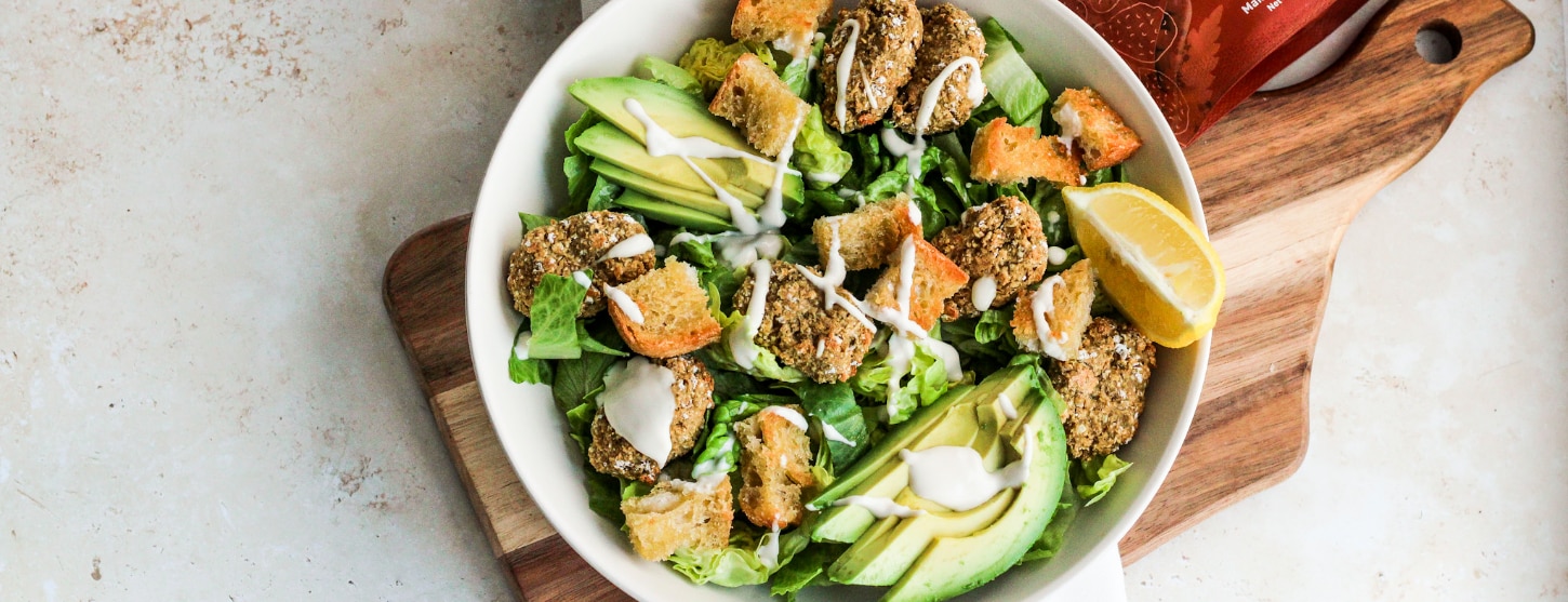 Vegan Caesar salad in bowl with vegan nuggets, creamy sauce, avocado and lemon
