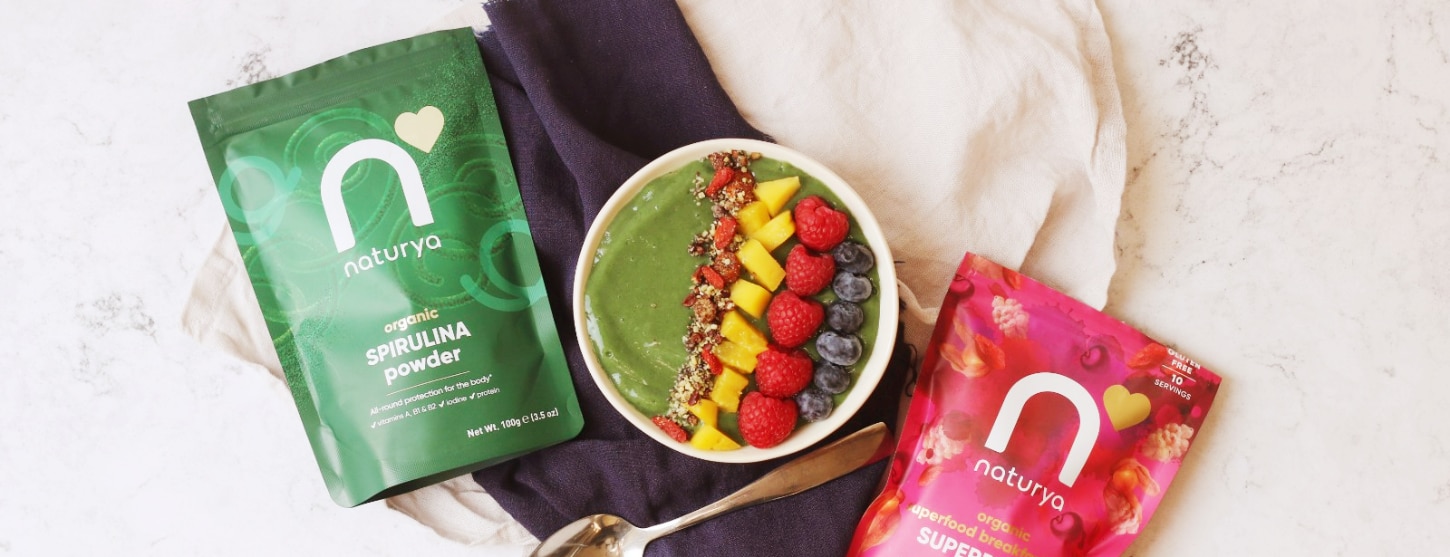 spirulina smoothie bowl topped with fresh mango, raspberries and strawberries next to Naturya products