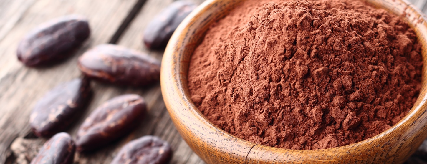 cacao powder in bowl next to cocoa beans