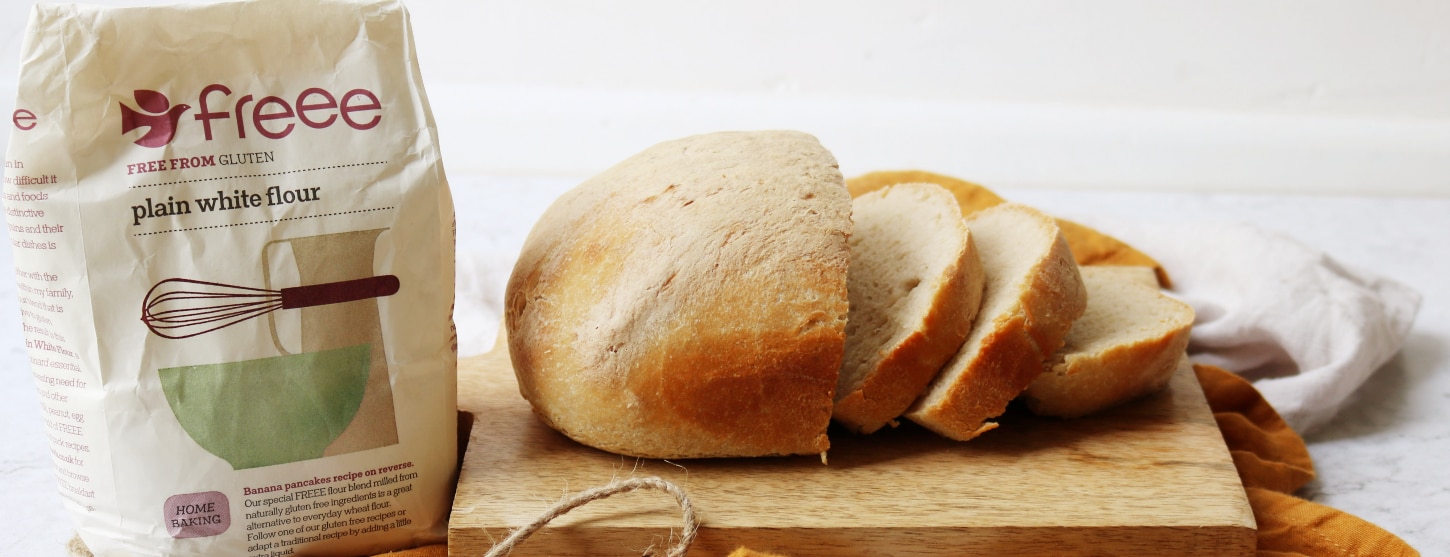gluten free bread loaf sliced on a bread board next to gluten free flour 