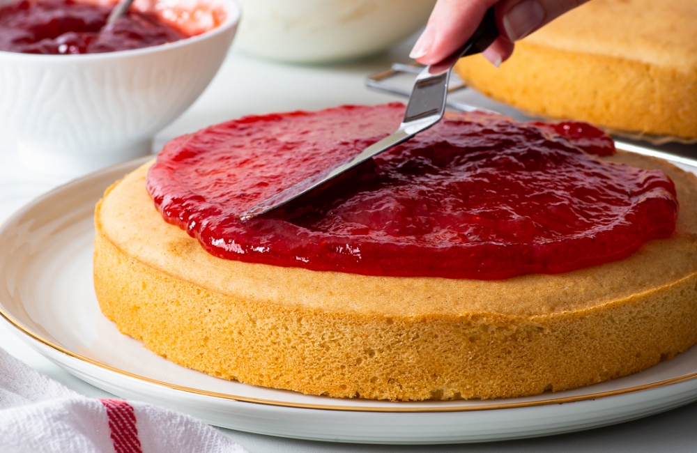 spreading jam onto baked vanilla sponge cake