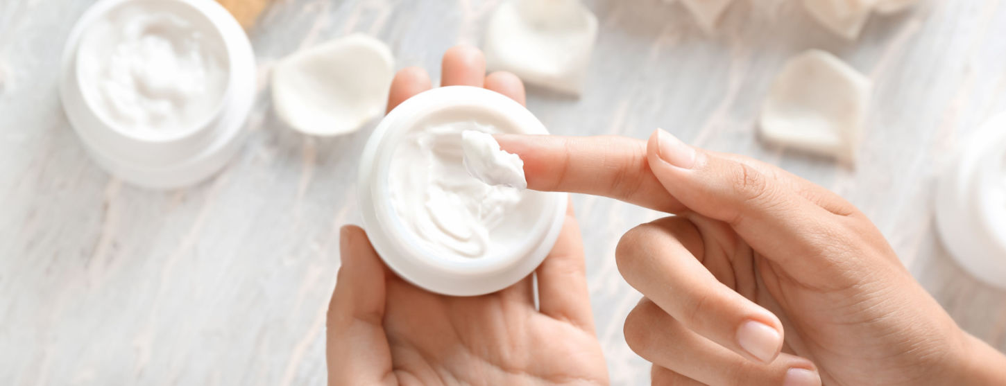a ladies hand holds a white pot of facial cream