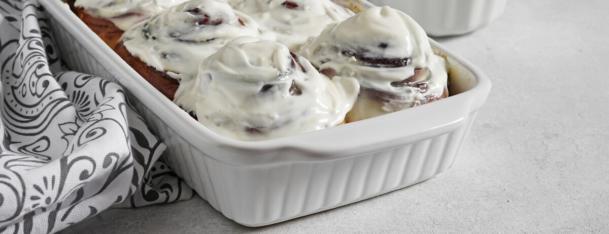 Cinnamon rolls on a cooling rack with a bowl of cream cheese frosting