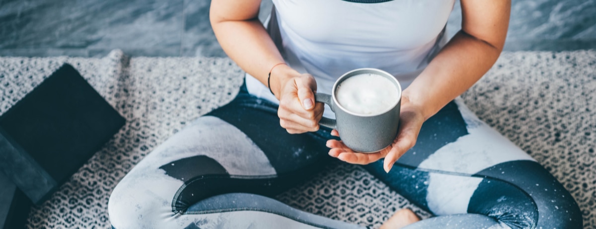 a woman in workout clothes sitting with a cup of coffee 