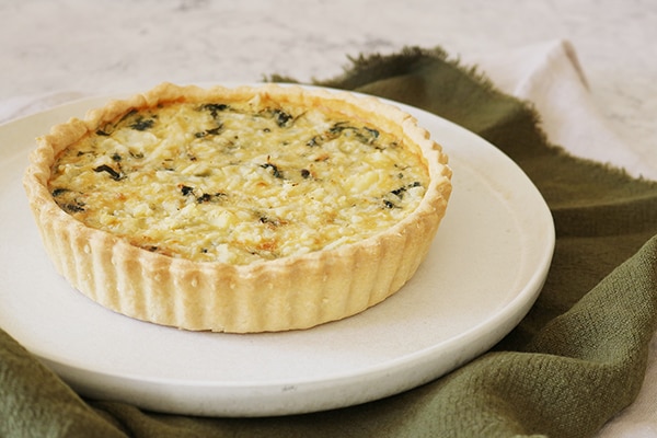 Portion of coronation quiche from the side in a white bowl on a green cloth