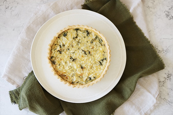 Portion of coronation quiche from above in a white bowl on a green cloth