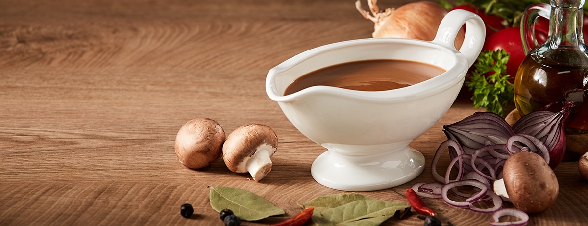 A pouring bowl containing vegan gravy with mushrooms on the side