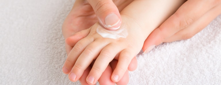 mothers hand putting lotion on baby hand 
