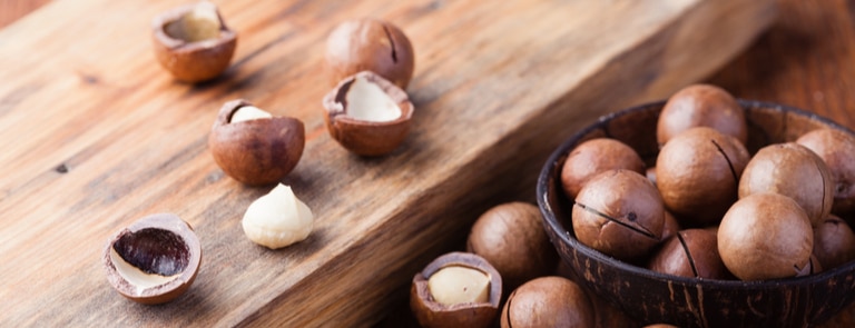 raw macadamia nuts on wooden table and bowl 
