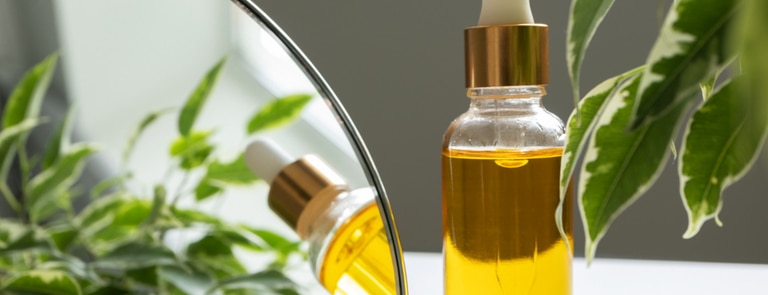 cosmetic bottle of moisturising oil next to green leaves 