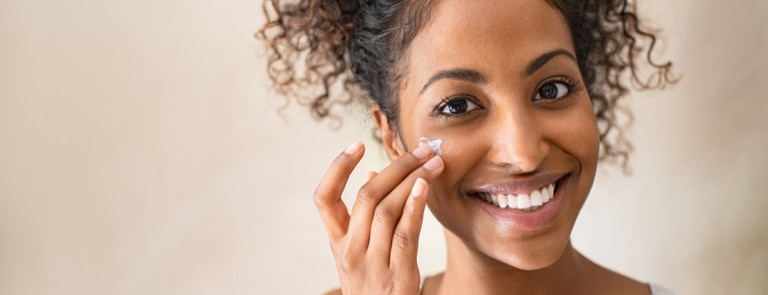 smiling woman applying moisturiser to face