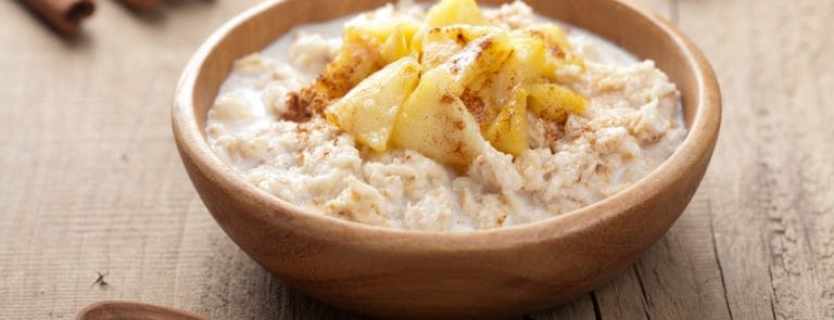 Porridge with apple and cinnamon in a wooden bowl against a wooden background
