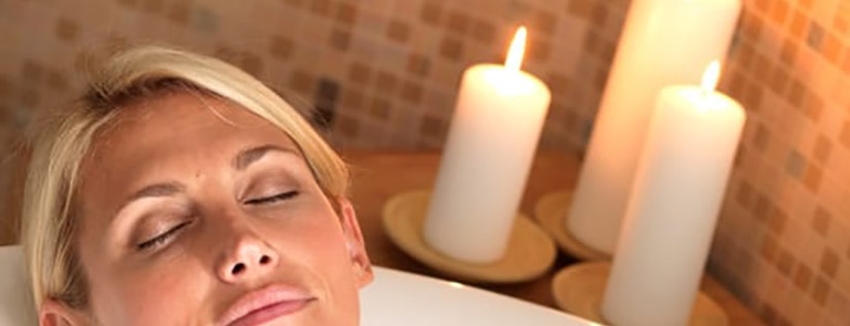 A women lay in a bath relaxing with candles in the background