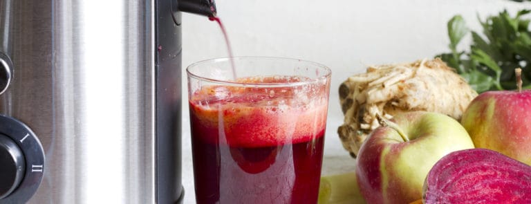 A juicer making a red juice with various ingredients next to it
