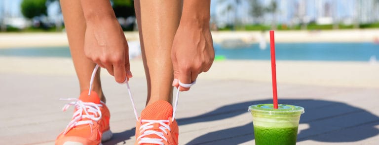 A women with a green smoothie tying her shoe laces