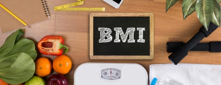 BMI written on a chalk board with fruit and veg, scales and office items near it