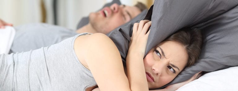 A man snoring next to a woman awake covering her ears with a pillow