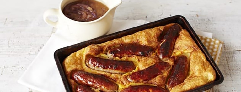 Toad in the hole in a baking tray with a jug of onion gravy