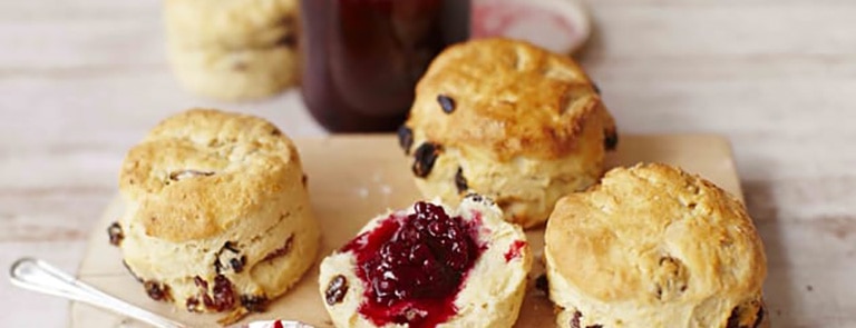 Fruit scones on a wooden chopping board with blackberry jam