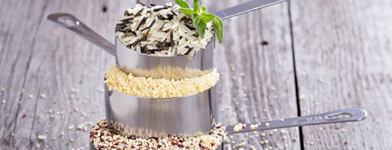 Three measuring cups with rice, grains and seeds in them