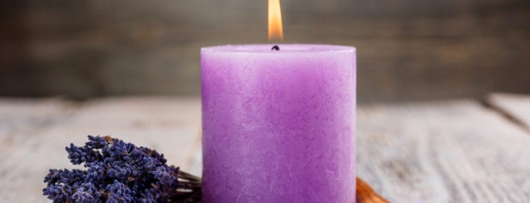 A purple lavender scented candle next to some lavender