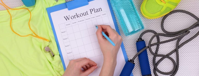 Someone writing in their workout plan with exercise equipment page
