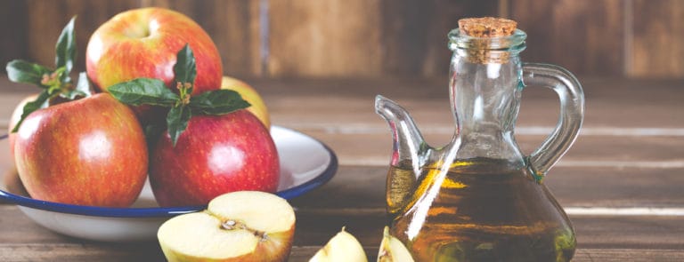 A bowl of Apples next to some apple cider vinegar